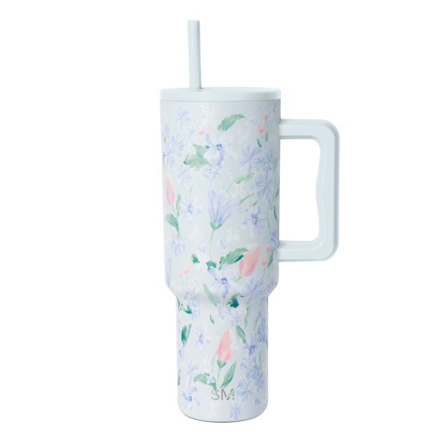 White insulated tumbler with periwinkle, lavender, and pink floral pattern, matching handle and straw, photographed against white background. White insulated tumbler with periwinkle, lavender, and pink floral pattern, matching handle and straw, photographed against white background.