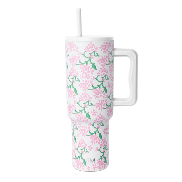 White insulated tumbler with handle and lid featuring pink flowers and green foliage pattern, Simple Modern logo, against white background. White insulated tumbler with handle and lid featuring pink flowers and green foliage pattern, Simple Modern logo, against white background.
