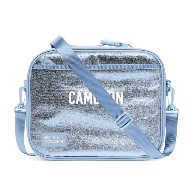 Simple Modern Cameron shoulder bag with silver metallic center panel and periwinkle blue handles, featuring top zippered closure and adjustable webbing strap against white background. Simple Modern Cameron shoulder bag with silver metallic center panel and periwinkle blue handles, featuring top zippered closure and adjustable webbing strap against white background.