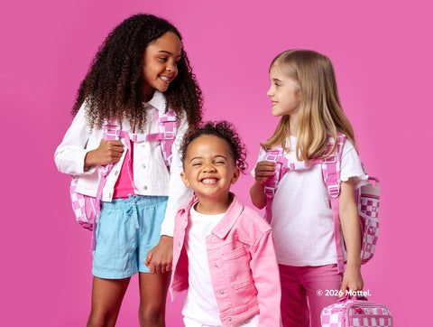Three smiling children wearing coordinating Barbie-inspired outfits with pink and white Simple Modern backpacks against a bright hot pink studio backdrop.