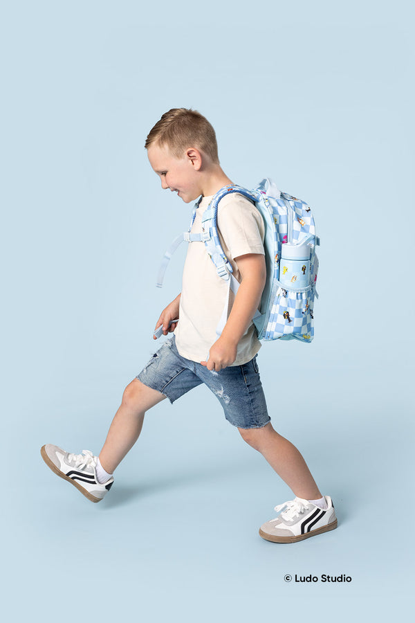 Boy in motion wearing cream t-shirt and blue shorts with Simple Modern Bluey collection backpack featuring blue and white gingham pattern and colorful character graphics against light blue background.