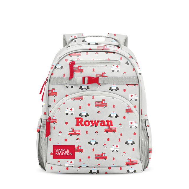 Simple Modern Rowan children's backpack with emergency vehicle print featuring red fire trucks, police cars, and fire hydrants on light gray base, multiple zippered pockets, padded straps, front-facing on white background.