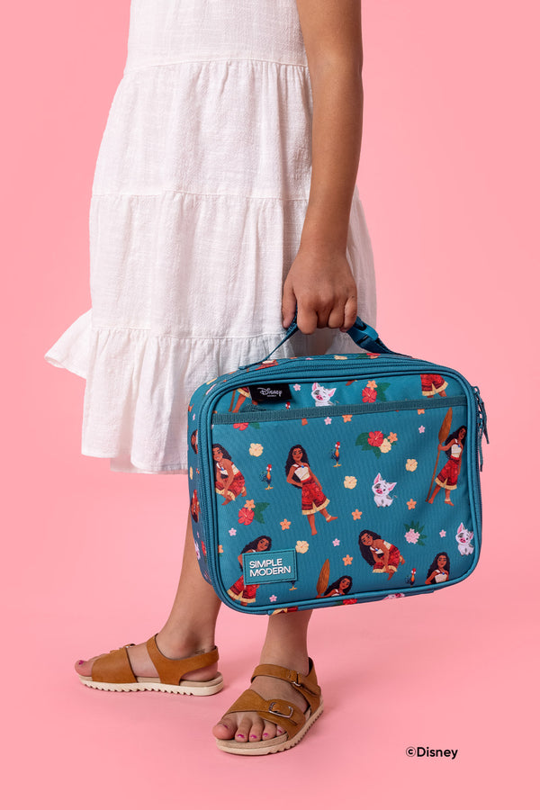 Person holding teal Simple Modern lunch box with Disney Princess characters on hot pink background, wearing white tiered dress and tan sandals.