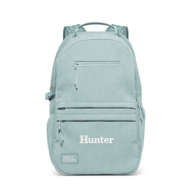 Sage green backpack with multiple zip pockets, padded straps, and top carry handle. Features 