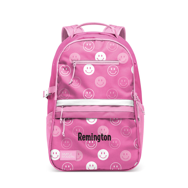 Hot pink children's backpack with white smiley face pattern, padded straps, front zippered pockets, white horizontal stripe, and mesh ventilation panels. Remington by Simple Modern brand.