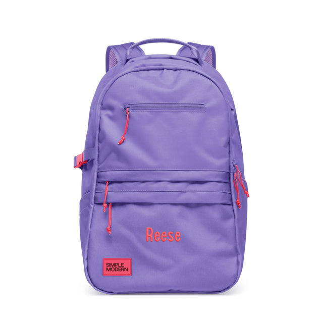 Periwinkle purple backpack with coral red accents, padded shoulder straps, multiple zippered pockets, and side compression straps. Features 