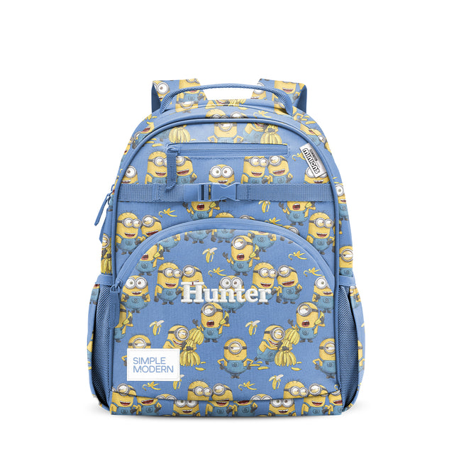 Periwinkle blue children's backpack with all-over Minion and banana print, featuring padded carry handle, front zippered pocket, side mesh pockets, and quick-release buckle strap. Simple Modern Hunter brand.