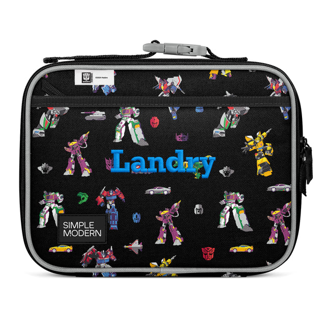 Black insulated Landry lunch box by Simple Modern featuring colorful Transformers characters, gray fabric handle, and side carry handles on white background.