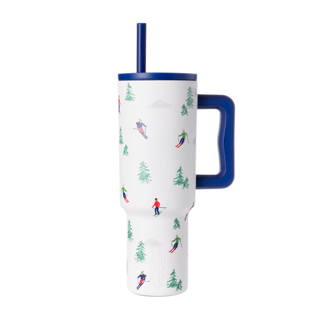 White insulated tumbler with navy blue lid, handle, and straw, featuring forest green evergreen tree design accents