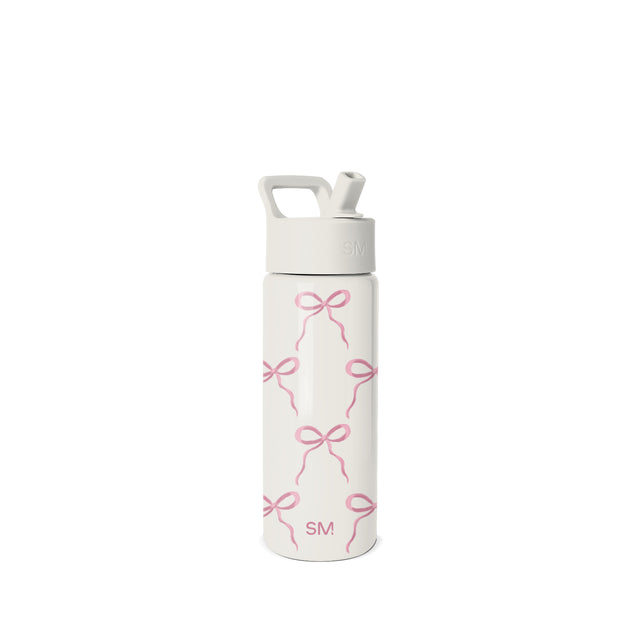 White and pink Simple Modern water bottle with straw cap, carry handle, and repeating bow pattern design. SM logo on cap and body. Studio product photo on neutral background.