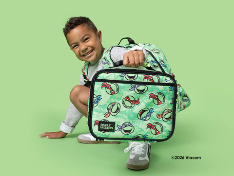 Child smiling and holding a Simple Modern lunch bag with ninja-themed cartoon graphics against a mint green background. The pastel green bag features black handles and zippered pockets.