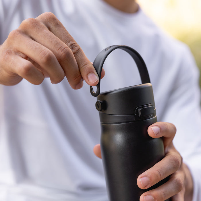 Close-up of two hands lifting the folding handle on a black bottle.